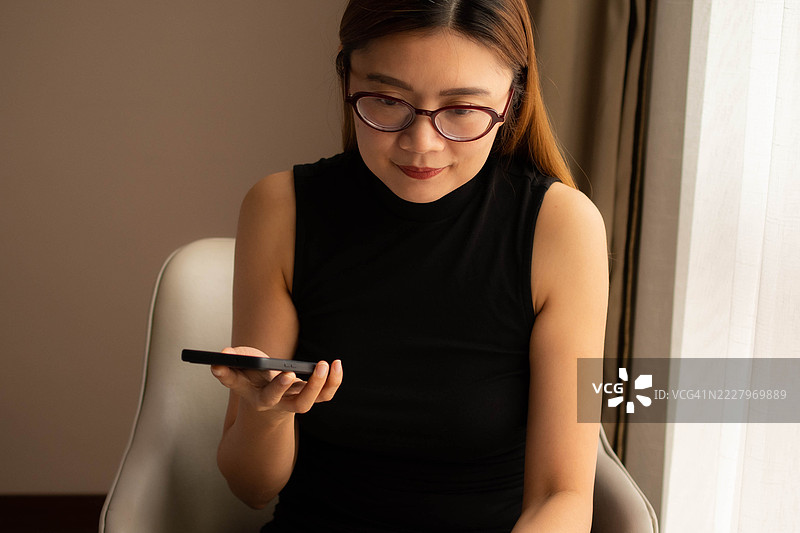 一位中年千禧一代的东南亚女性在家中使用智能手机——通过用户友好的应用程序和平台检查余额、进行交易和管理预算。图片素材