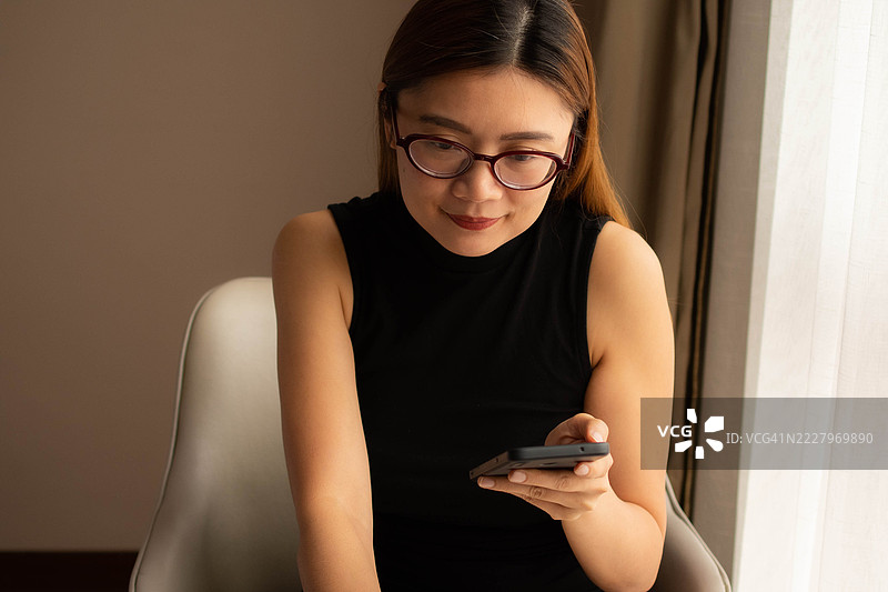 一位中年千禧一代的东南亚女性在家中使用智能手机——通过用户友好的应用程序和平台检查余额、进行交易和管理预算。图片素材