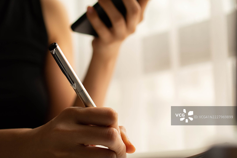 一位中年千禧一代的东南亚女性在家中使用智能手机——通过用户友好的应用程序和平台检查余额、进行交易和管理预算。图片素材