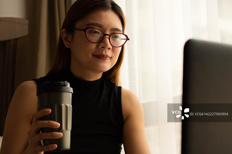 一位中年千禧一代的东南亚女性在家中使用笔记本电脑——通过用户友好的应用程序和平台检查余额、进行交易和管理预算。图片素材