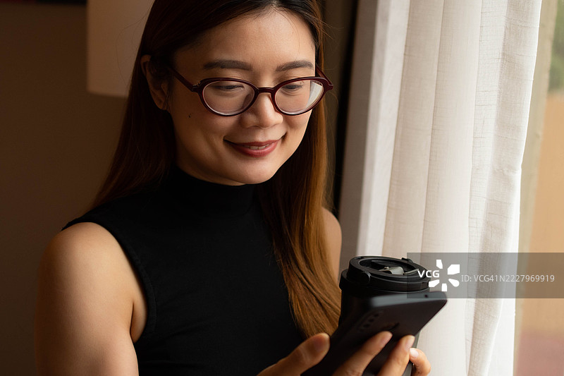 一位中年千禧一代的东南亚女性在家中使用智能手机——通过用户友好的应用程序和平台查看余额、进行交易和管理预算。图片素材