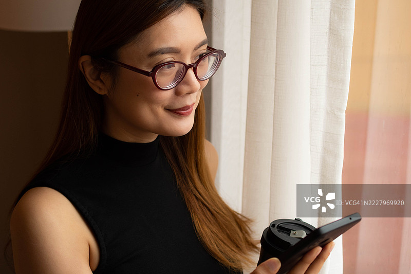 一位中年千禧一代的东南亚女性在家中使用智能手机——通过用户友好的应用程序和平台检查余额、进行交易和管理预算。图片素材