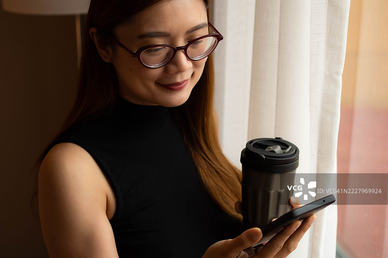 一位中年千禧一代的东南亚女性在家中使用智能手机——通过用户友好的应用程序和平台检查余额、进行交易和管理预算。图片素材