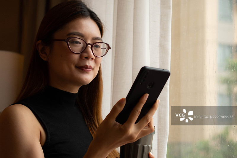 一位中年千禧一代的东南亚女性在家中使用智能手机——通过用户友好的应用程序和平台检查余额、进行交易和管理预算。图片素材