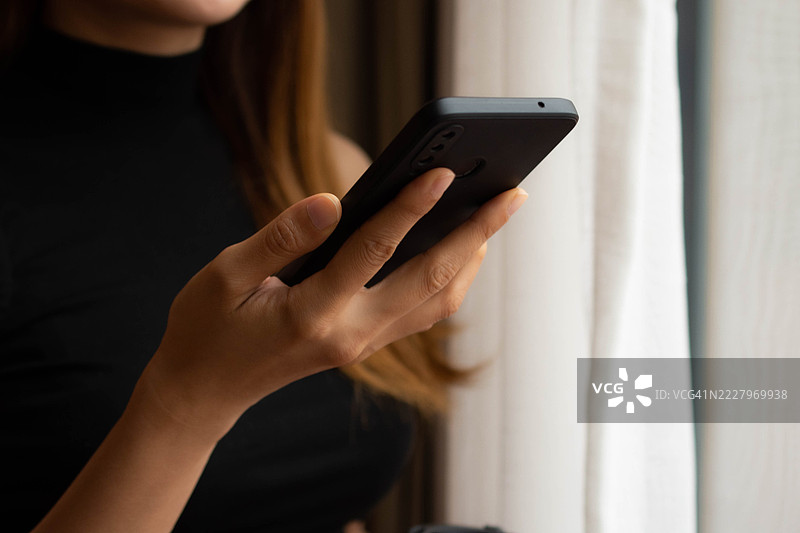 一位中年千禧一代的东南亚女性在家中使用智能手机——通过用户友好的应用程序和平台检查余额、进行交易和管理预算。图片素材