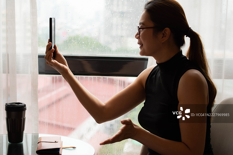 一位中年千禧一代的东南亚女性在家中使用智能手机——通过用户友好的应用程序和平台检查余额、进行交易和管理预算。图片素材