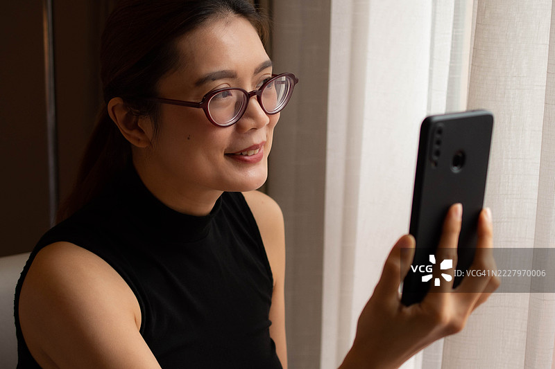 一位中年千禧一代的东南亚女性在家中使用智能手机——通过用户友好的应用程序和平台检查余额、进行交易和管理预算。图片素材