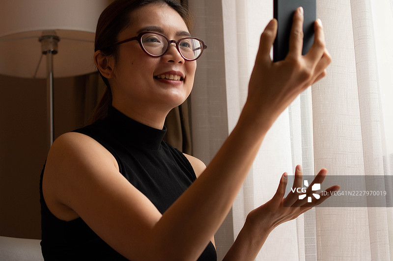 一位中年千禧一代的东南亚女性在家中使用智能手机——通过用户友好的应用程序和平台检查余额、进行交易和管理预算。图片素材