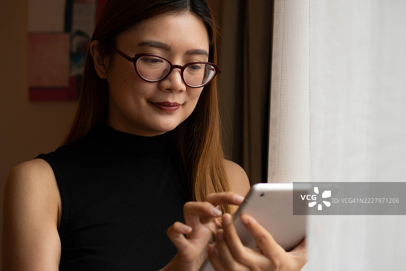 一位中年千禧一代的东南亚女性在家中使用数字平板电脑——通过用户友好的应用程序和平台检查余额、进行交易和管理预算。图片素材