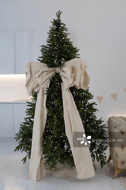 装饰着灯光和大布条的圣诞树，矗立在极简室内环境中的沙发旁。图片素材