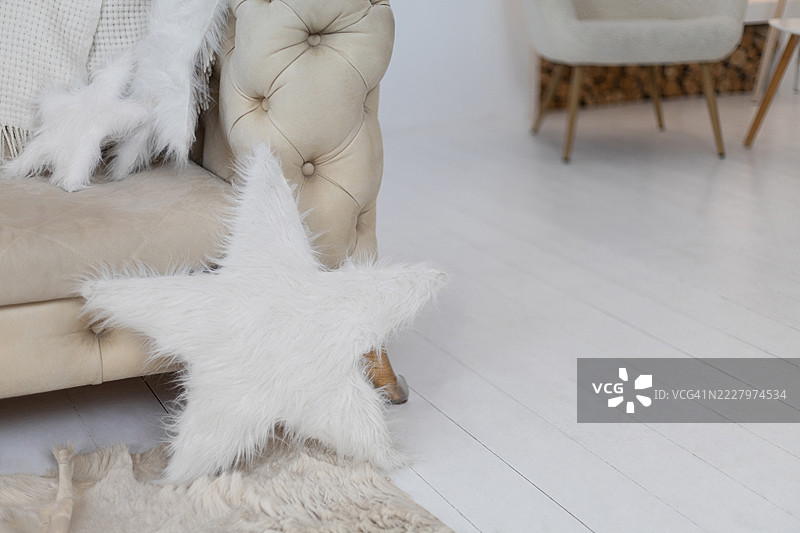 白色星形毛绒靠垫和一块仿毛皮地毯，放在一张带有绗缝的米色沙发旁，沙发上有一条柔软的毛毯。图片素材