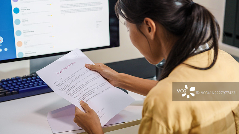 沮丧的被解雇女性在家中阅读粉色解雇信，因经济衰退和公司裁员，公司面临严重的财务问题，她被裁员，失业概念。图片素材