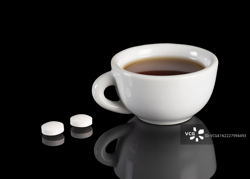黑色背景上反射着一杯热茶和两颗止痛药。图片素材