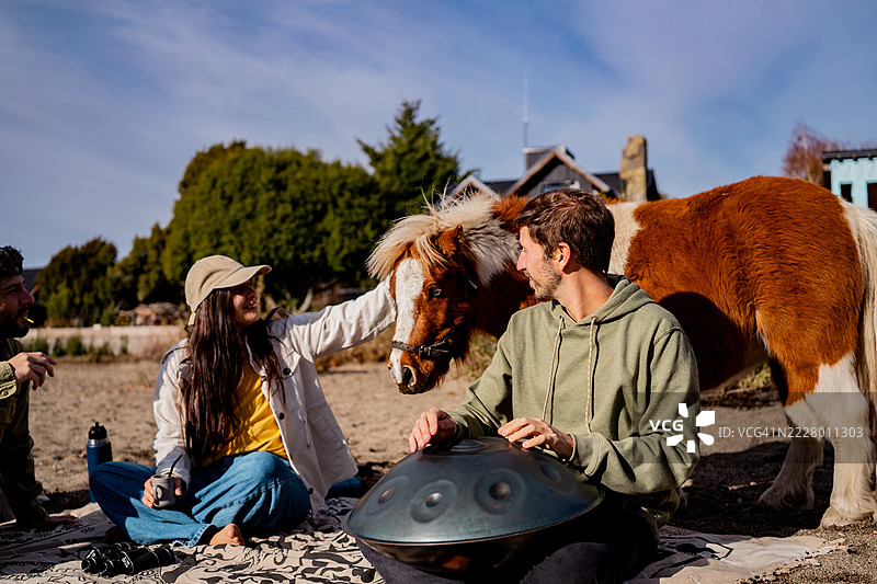 朋友们在阿根廷巴塔哥尼亚抚摸小马，同时演奏手盘。图片素材