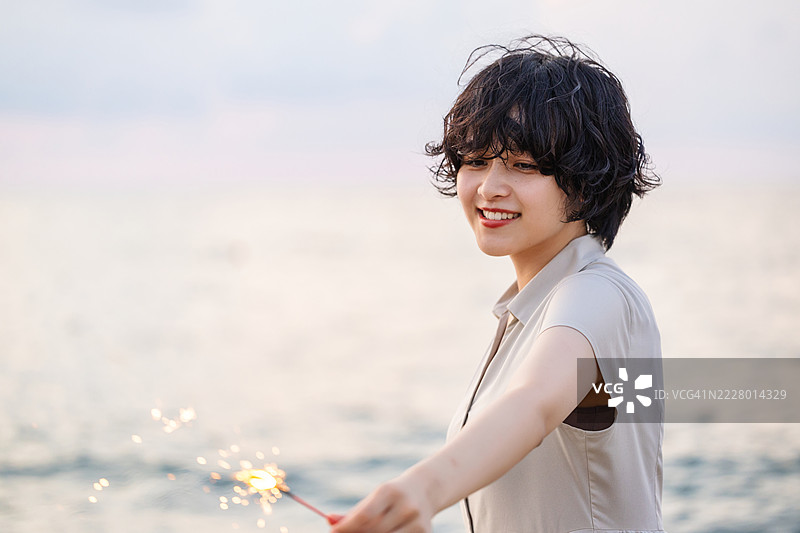 一位女性模特在黄昏时分的海滩上享受烟花，采用柔和的模糊效果。图片素材