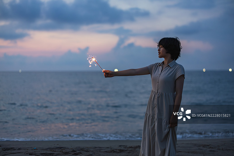 一位女性模特在黄昏时分的海滩上享受烟花，使用柔和的模糊效果。图片素材