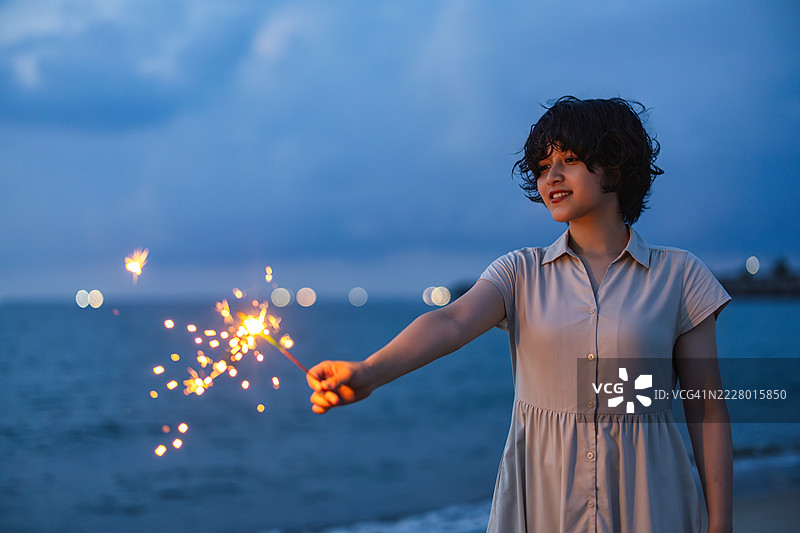 一位女性模特在黄昏时分的海滩上享受烟花，采用柔和的模糊效果。图片素材