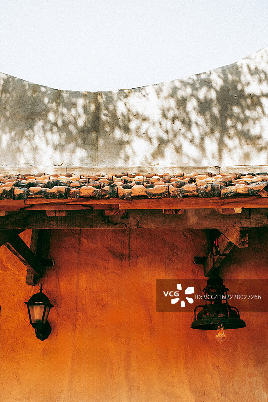 带有橙色灰泥的乡村墙壁和古老的瓦屋顶，配有复古黑色灯笼和悬挂在木梁下的灯，表面上洒落着柔和的光影。图片素材