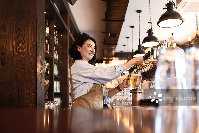 女调酒师在酒吧后面倒生啤酒图片素材
