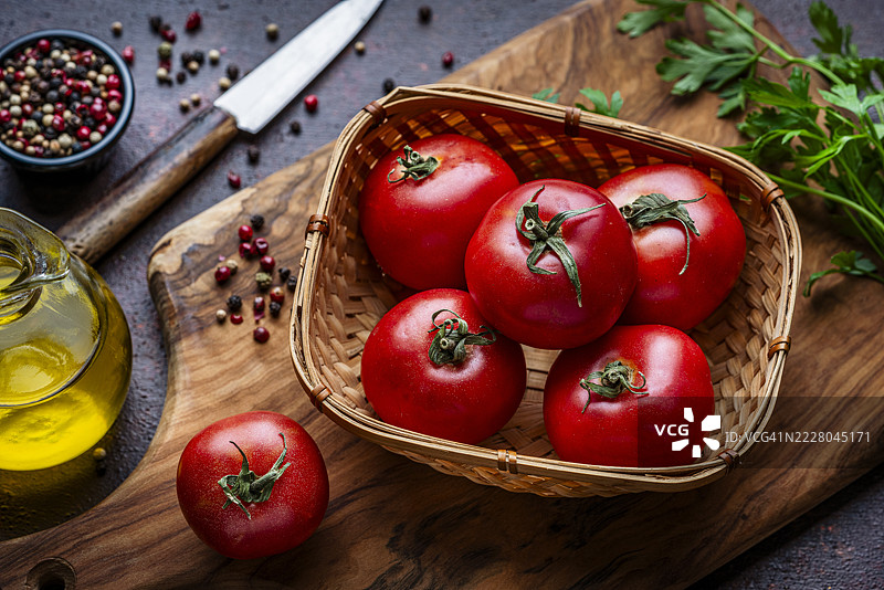 成熟的有机番茄放在藤编篮子里，置于木质切菜板上。烹饪或准备素食饮食。地中海美食。俯视图。图片素材