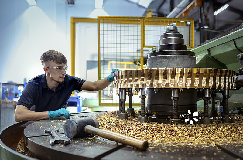 工程师在工厂检查机器上的黄铜齿轮图片素材