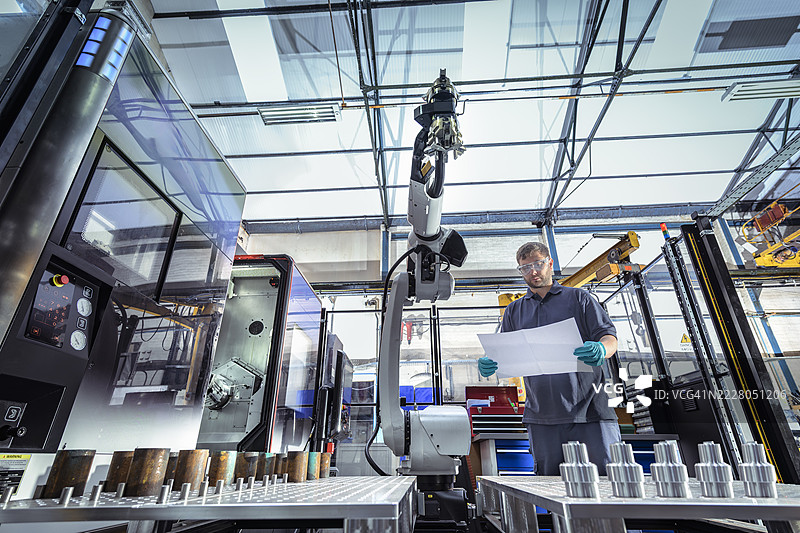 工程师在工厂中查看图纸，旁边有机器人和数控车床图片素材