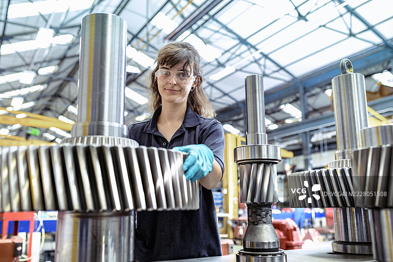 女性工程师在工程工厂的工作台上操作大型钢齿轮图片素材