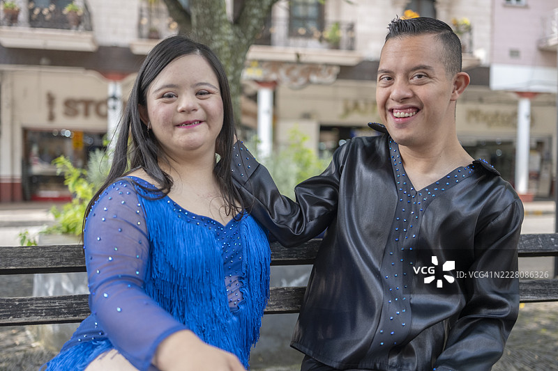 一对年轻的唐氏综合症情侣坐在长椅上，享受户外生活。图片素材