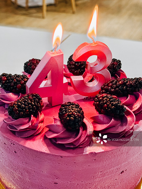 粉色生日蛋糕，上面点燃的蜡烛和黑莓，庆祝43岁生日图片素材