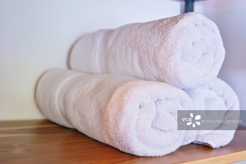 木架子上的卷白毛巾，背景为白色墙壁图片素材