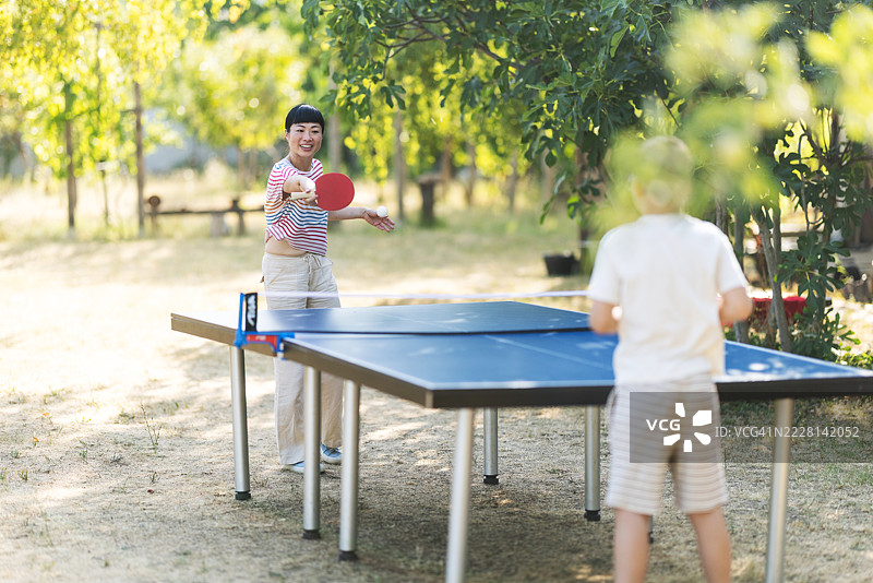 快乐的女人在后院与一个男孩打乒乓球图片素材