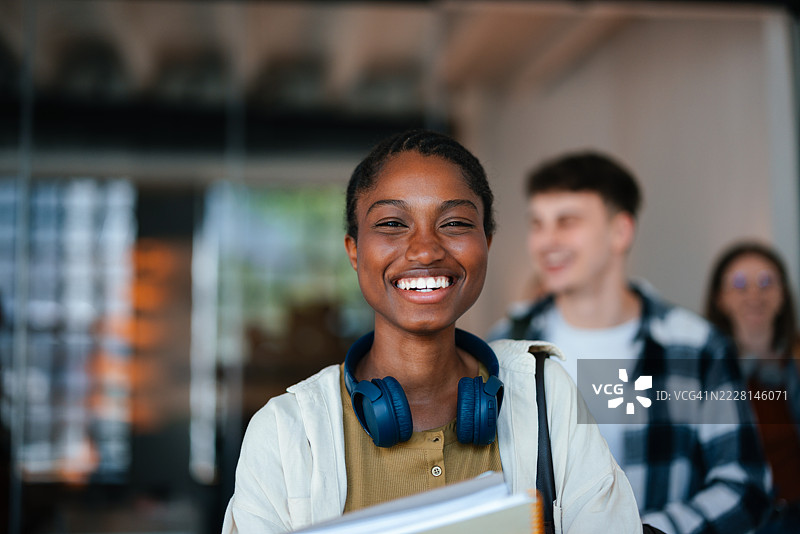 微笑的学生戴着耳机，身边围绕着朋友们，在学校环境中。图片素材