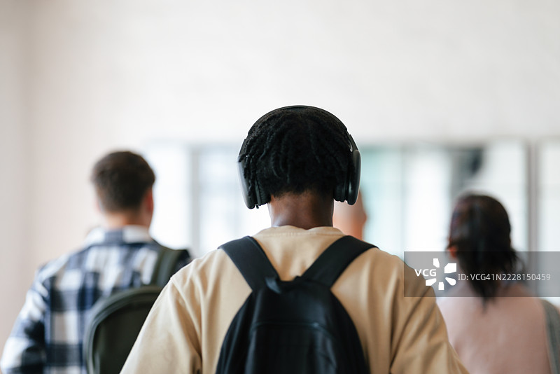 学生们在校园环境中背着书包，戴着耳机一起走路图片素材