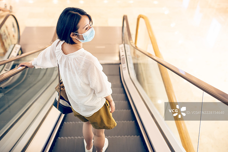 一位戴着口罩的亚洲女性站在扶梯上图片素材