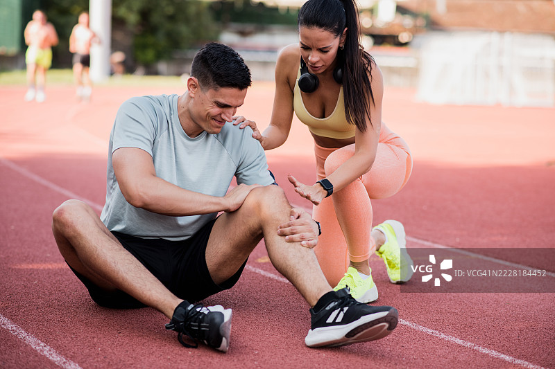 担心的年轻女性在跑道上帮助受伤的男性图片素材
