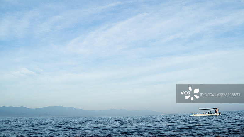 一只小船在巴厘海上航行，驶向巴厘岛，背景是蓝色的天空。图片素材