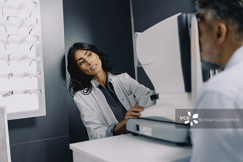 女性眼科医生在现代眼科诊所使用诊断设备为一位老年男性患者进行眼部检查。图片素材