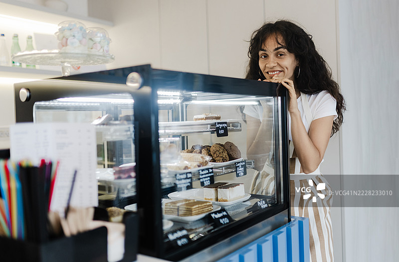 在蛋糕展示柜旁工作的女性面包师图片素材