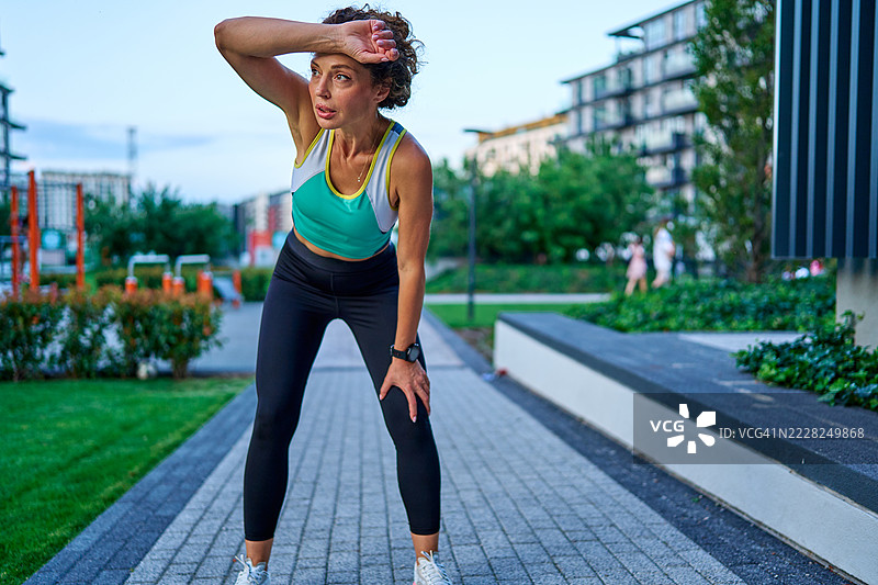 疲惫的女运动员在城市公园跑步后擦去额头上的汗水图片素材