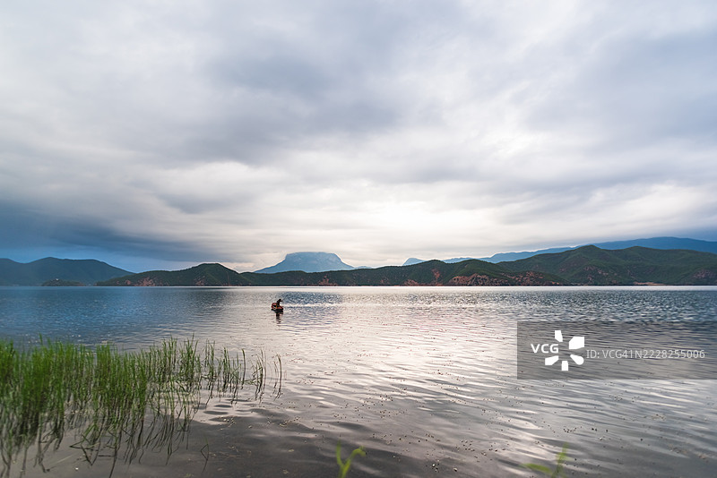 宁静的湖泊，远处山脉在阴云密布的天空下，旁边有一个人。图片素材