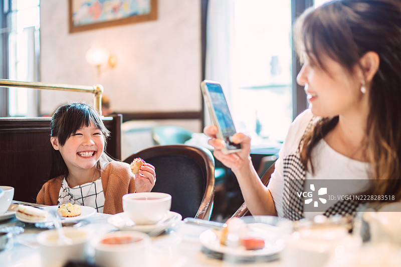 母亲在咖啡馆为女儿拍照，享受下午茶时光图片素材