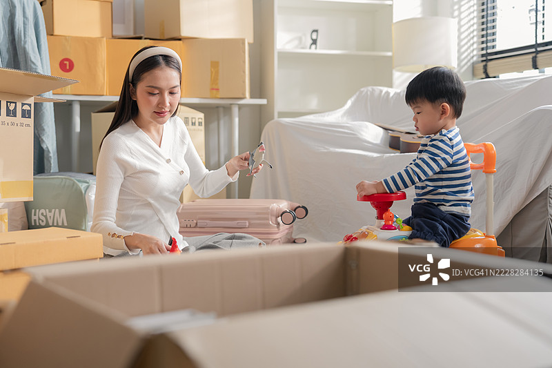 亚洲家庭在新家搬家，成年母亲正在拆包裹，而她的幼儿儿子在周围玩着小车玩具，一起度过搬家的时光。图片素材