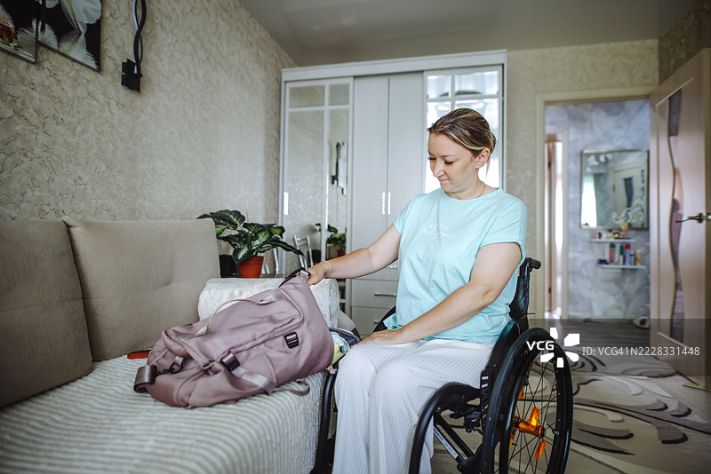 坐在轮椅上的女性在家中的客厅里，旁边有一个旅行包。图片素材