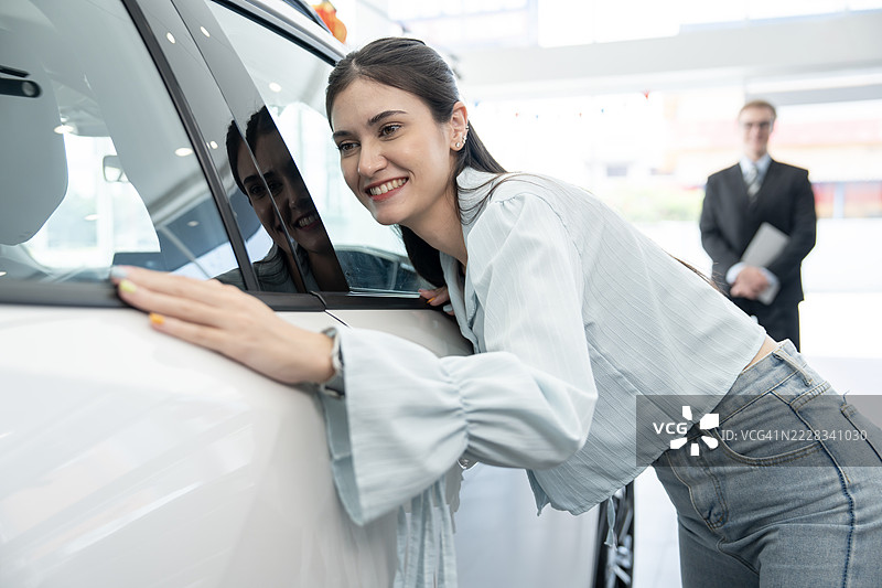 快乐的女性在展厅中分析汽车外观。图片素材
