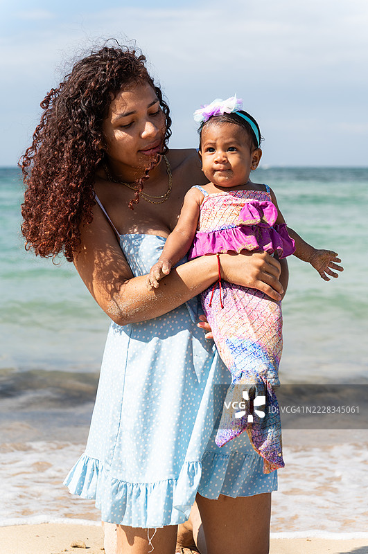 母亲在海滩上抱着穿着美人鱼服装的女儿图片素材