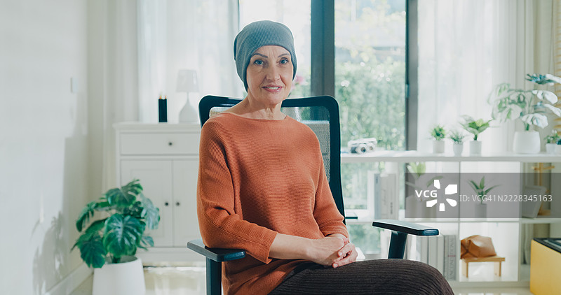 戴头巾的老年女性癌症患者在家中的沙发上分享她的癌症康复故事，通过播客讲述。与癌症共存的概念。图片素材