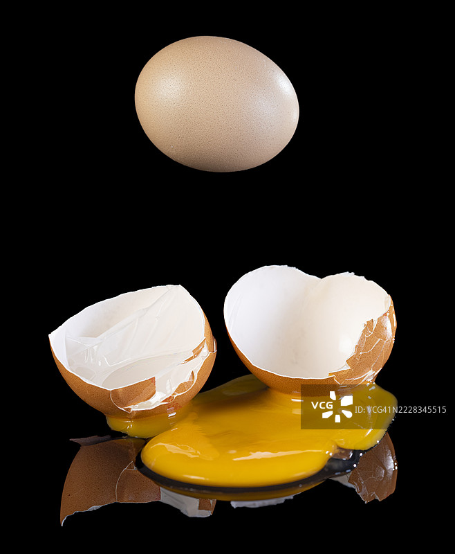 两只鸡蛋破裂，蛋黄洒落在黑色背景上。图片素材