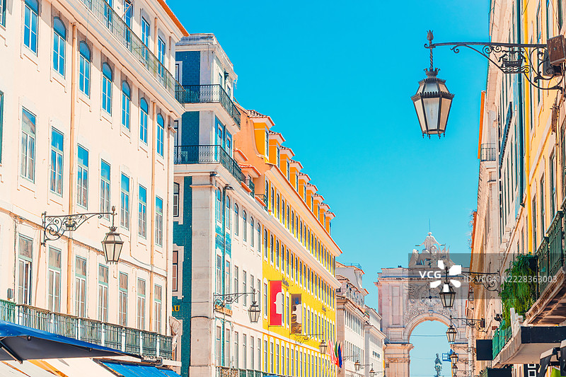 里斯本的奥古斯塔街拱门，一座宏伟的新古典主义凯旋门，装饰着华丽的雕塑和时钟，背景是色彩斑斓的历史建筑，映衬在晴朗的蓝天之下。图片素材