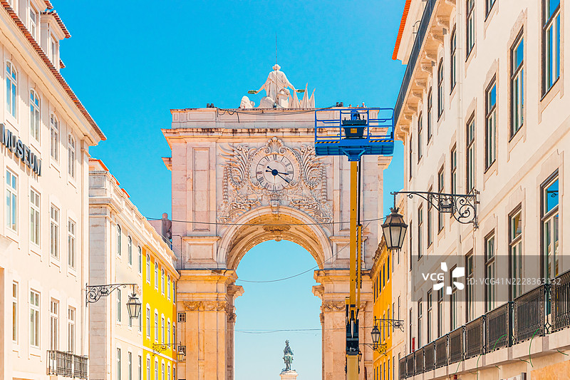 里斯本的奥古斯塔街拱门，一座宏伟的新古典主义凯旋门，装饰着华丽的雕塑和时钟，背景是色彩斑斓的历史建筑，映衬在晴朗的蓝天之下。图片素材