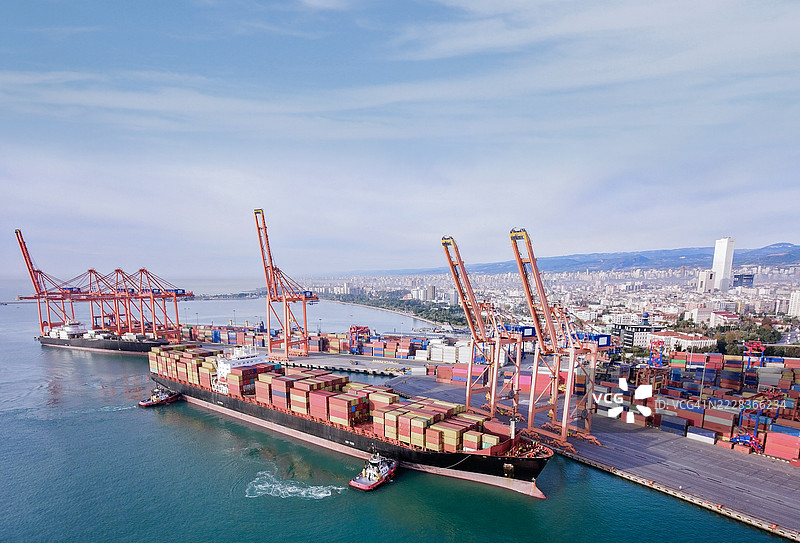 货运集装箱船在拖船的引导下驶向港口的鸟瞰图。图片素材